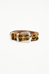 Cinturón de cuero vacuno con acabado de pelo animal print, de 2,5 cm de ancho. Presenta remaches metálicos en forma de corazón, hebilla, pasador y puntera metálica en tono plata.