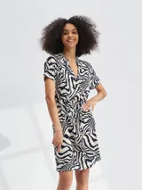 Vestido corto con estampado animal print tipo cebra en tonos blanco y negro. Presenta escote en V, mangas cortas y un lazo ajustable en la cintura para entallar la silueta.