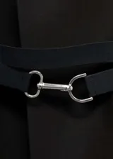 Abrigo largo estructurado de corte recto, color negro, con cuello de solapa, manga larga y cinturón desmontable con cierre metálico. Presenta bolsillos de ribete y solapa, y una abertura posterior en el bajo.