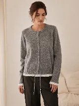 Cardigan de punto gris con cuello redondo y cierre frontal de botones. Presenta detalles de puntilla blanca en el bajo y en los puños, además de un lazo ajustable en la cintura.