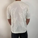 Camisa de tejido de punto calado color negro, con cuello solapa, cierre frontal de botones y mangas cortas.