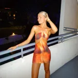 Vestido corto ajustado con diseño cut-out en la cintura y escote halter. Presenta un estampado abstracto con tonos cálidos de naranja, rojo y marrón.