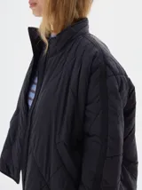 Campera marrón claro con diseño acolchado de rombos, cuello alto, cierre frontal con cremallera, bolsillos laterales y mangas largas con rayas blancas.