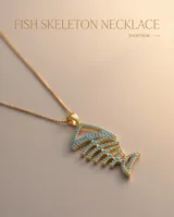 Collar de bronce en tono dorado con una fina cadena y un dije colgante en forma de espina de pescado, decorado con circonias de color turquesa.