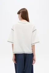 Remera de algodón color crudo, con cuello redondo a la base, mangas 3/4 holgadas y costuras con pespuntes en tono contrastante.