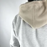 Canguro gris melange de algodón con felpa, capucha y bolsillo tipo sobre. Presenta cordón beige y logo Duxon bordado en el pecho.