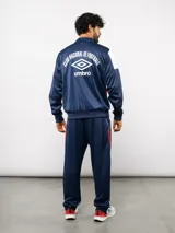 Conjunto deportivo Umbro del Club Nacional de Football, compuesto por una campera con cierre frontal y un pantalón a juego. Ambas piezas son de color azul marino con detalles en blanco y rojo, presentando el escudo del club y el logo de la marca.