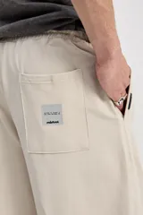 Pantalón de algodón color beige, de corte holgado y pierna amplia, con cintura elastizada y cordón ajustable.