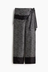 Pantalón negro con estampado de lunares blancos, corte recto y falda cruzada superpuesta con lazada en el lateral.