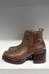 Bota corta de cuero color marrón, con diseño de punta cuadrada y taco cuadrado con textura grabada. Presenta costuras visibles y una lengüeta en la parte posterior.