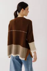 Buzo de lana color beige con bloques de color ocre y bordó en mangas y ruedo. Presenta un bolsillo pequeño en el pecho y costuras decorativas en color bordó.