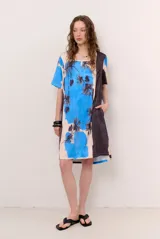 Vestido corto de corte recto y holgado, con mangas cortas y cuello redondo. Presenta un diseño estampado con motivos florales oscuros y una franja lateral en tono contrastante.