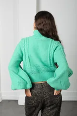 Polera de punto color verde menta, con cuello alto, mangas globo y diseño de trenzas en el frente.