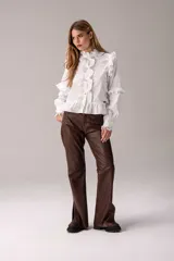 Camisa negra de corte entallado con volados decorativos en el cuello, la botonadura frontal, los hombros y las mangas. Presenta mangas largas con puños ajustados y un ruedo con volado inferior.