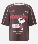 Remera de algodón color marrón con cuello redondo y mangas cortas. Presenta un estampado frontal con el personaje Snoopy en temática de carreras y detalles de líneas blancas contrastantes en los hombros y mangas.