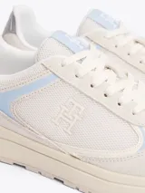 Zapatillas deportivas Tommy Hilfiger de corte bajo, color blanco con detalles en celeste y plateado. Presentan paneles de malla y superposiciones de gamuza, con el monograma TH en la lengüeta y el lateral.