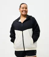 Campera cortavientos deportiva de Ashua, con diseño bicolor en negro y blanco. Presenta capucha integrada ajustable, cierre frontal con cremallera, mangas largas con puños elásticos y cintura elástica. Confeccionada en poliamida con forro de poliéster.