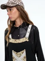 Mono largo de color negro con corte holgado y perneras anchas. Presenta detalles de encaje blanco y tela estampada floral en los tirantes, el bolsillo frontal, la parte inferior de las piernas y el ruedo.