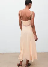 Vestido midi de estilo lencero color salmón, con detalles de encaje en el escote en pico y bajo el busto. Cuenta con tirantes finos ajustables, diseño evasé y forro interior.