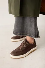 Zapatilla urbana de cuero marrón con paneles de gamuza al tono. Presenta suela de goma color crema, cordones bicolores trenzados y diseño de puntera reforzada.