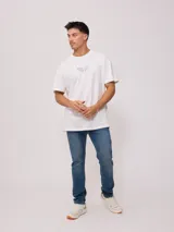 Remera de algodón con efecto lavado, corte oversized, manga corta y cuello redondo. Presenta un pequeño estampado gráfico en el pecho con texto y un diseño más grande en la espalda.