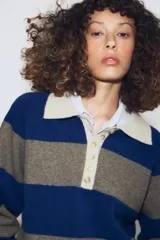 Jersey de punto a rayas horizontales azules y grises, con cuello tipo polo en color beige y cierre frontal con botones.