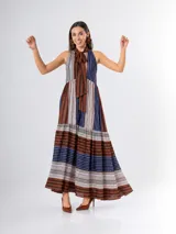 Vestido largo de organdí con diseño de rayas verticales en tonos marrón, azul y blanco en la parte superior y horizontales en la falda. Cuenta con escote halter y un lazo para atar en el cuello.