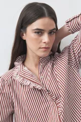 Camisa de manga larga a rayas verticales en tonos blanco y bordó, con cuello alto y detalle de volados frontales. Presenta puños con volados y un corte fluido.