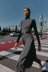 Vestido midi jaspeado en tonos grises, con cuello redondo, manga sisa y bajo en evasé. Incluye un cinturón ancho negro con hebilla rectangular y cierre de cremallera oculta en la espalda.