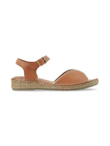 Sandalia plana de cuero color tostado con pulsera ajustable al tobillo y suela revestida en yute trenzado.