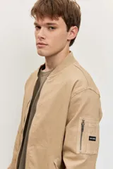 Campera bomber de gabardina color tostado, con cierre frontal y bolsillos laterales, puños y cintura elastizados de rib.