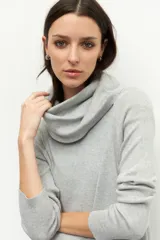 Polera gris de cuello extendible, manga larga y pequeñas aberturas en los laterales. Es suave y elastizada.