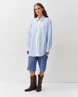 Camisa de corte recto y silueta ligeramente oversize, color celeste, con cuello clásico, cierre frontal de botones, bolsillo aplicado en el pecho y bajo redondeado.