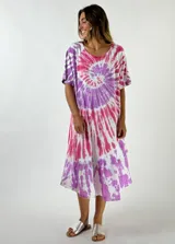 Vestido midi de algodón con estampado tie-dye en espiral de colores fucsia, violeta y blanco. Tiene escote redondo, mangas cortas y un volado en el ruedo.