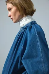 Campera bomber oversize de denim azul, con cuello elevado fruncido, cierre frontal y bolsillos laterales. Cuenta con mangas raglán y elásticos en puños y bajo.