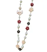 Collar largo compuesto por perlas de diferentes formas intercaladas con apliques de flores y moños de resina esmaltada en tonos rojo, negro y crema. Cuenta con cadena de alargue metálica.