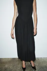 Vestido largo sin mangas con cuello subido, confeccionado con una parte superior lisa y falda de tul con caída fluida. Cuenta con cierre de cremallera oculta en la espalda.