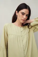 Camisa celeste de corte holgado con botones frontales, canesú con tablas y mangas 3/4 amplias con puño elastizado.