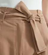 Pantalón cargo de tiro medio color beige, con cintura alta fija, cinturón ajustable para anudar, bolsillos laterales con solapa y botones, recortes verticales en las piernas y cierre frontal con botón y cremallera.