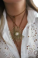 Collar con gargantilla de cuero marrón y dije dorado en forma de sol con piedra nacarada en el centro.