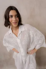 Camisola blanca de silueta amplia y caída liviana, con bordados florales sutiles, cuello camisero, cierre frontal de botones y mangas 3/4.