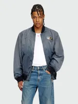 Campera bomber Diesel modelo J-Kepes, color gris azulado con efecto desgastado. Presenta cuello, puños y ruedo en tejido acanalado negro, cierre frontal y un distintivo logo metálico ovalado en el pecho.