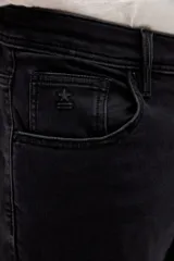 Jean de corte slim, color negro, con diseño de cinco bolsillos, cierre frontal con botón y cremallera.