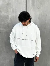 Canguro blanco con capucha ajustable con cordones, bolsillo tipo canguro y logo estampado en el pecho.