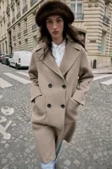 Abrigo largo cruzado color gris oscuro, confeccionado con lana. Presenta cuello solapa, manga larga, bolsillos delanteros de plastrón y cierre frontal con botones.