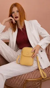 Bandolera pequeña tipo porta celular, color amarillo, confeccionada en símil cuero. Cuenta con cierre principal, bolsillo frontal con tapa y broche a presión, y correa larga ajustable.