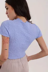 Blusa lavanda de mangas cortas con textura arrugada y cuello alto.
