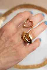 Par de aros asimétricos dorados de acero quirúrgico. Uno con forma de corazón y otro con forma de labios.