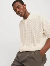 Polo loose de tejido estructurado color beige, con cuello tipo polo, mangas cortas, hombros caídos y cierre frontal con botones.