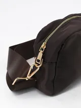 Bandolera de diseño rectangular en color chocolate, confeccionada en material sintético con acabado liso. Cuenta con cierre superior, correa ajustable al tono y un detalle circular decorativo en el centro del frente.